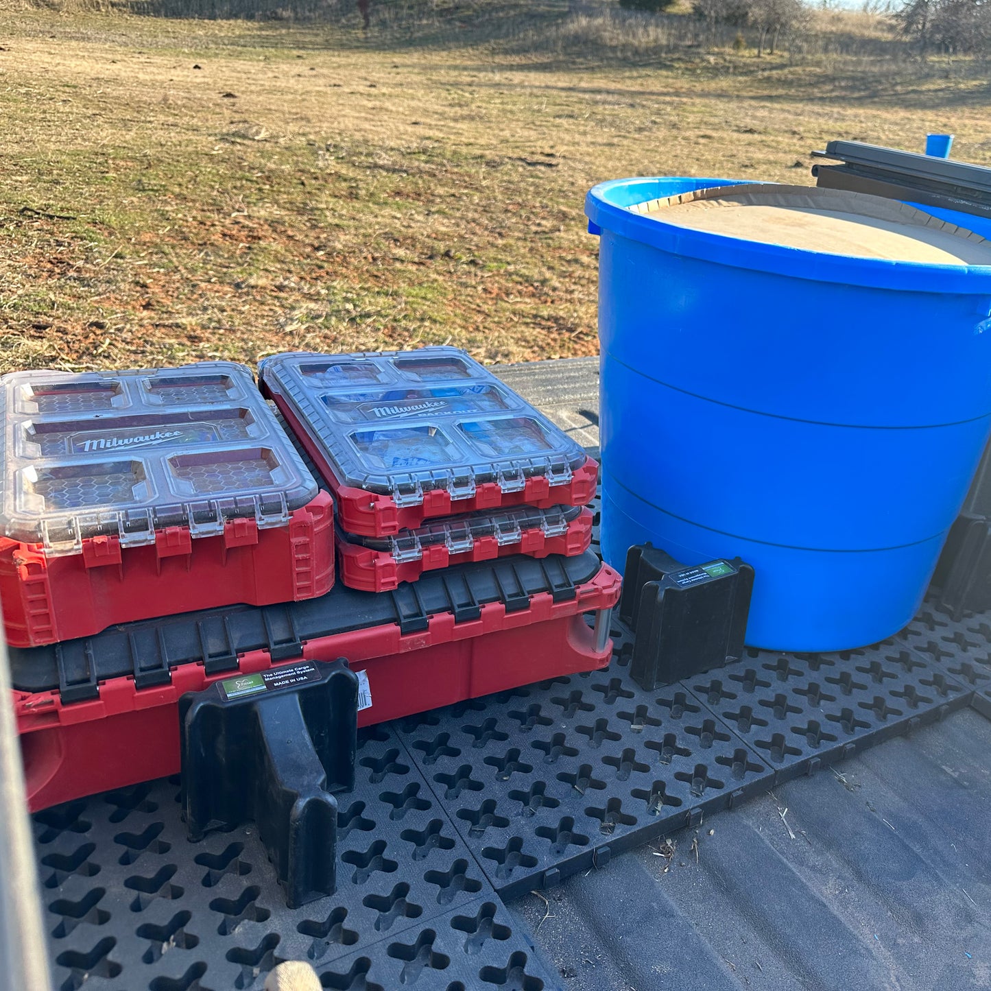 Tool boxes and a protein tube sitting on Tmat in the back of a pickup on a farm.