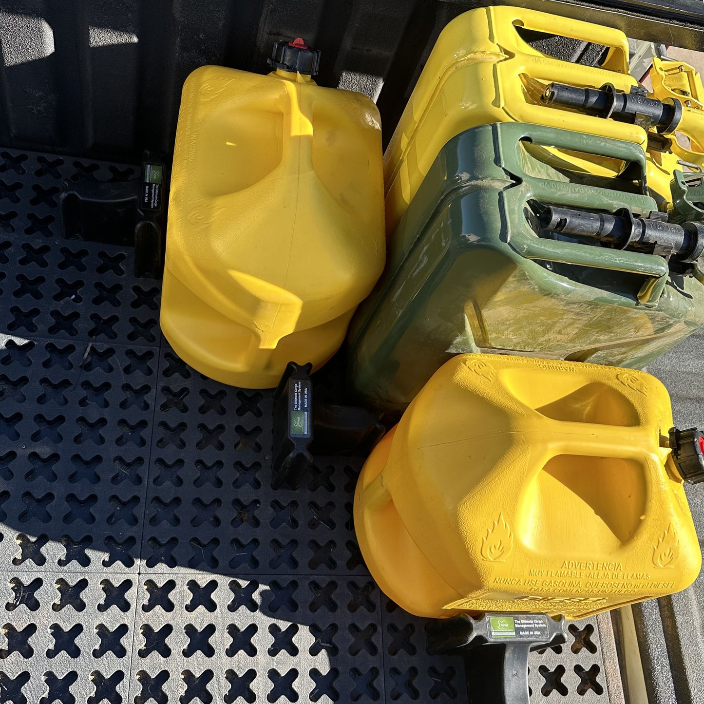 Metal jerry cans and plastic gas cans are secured for transport with Tmat in the back of a pickup truck.