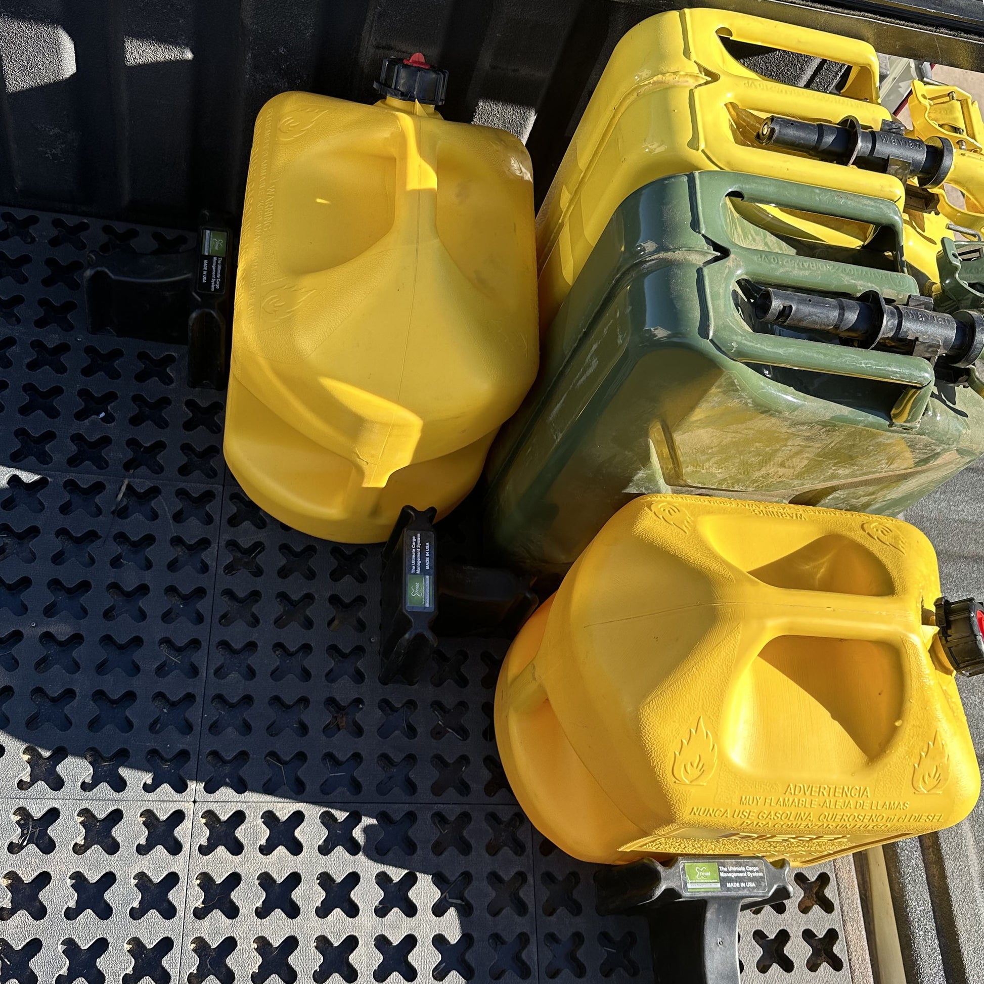 Metal jerry cans and plastic gas cans are secured for transport with Tmat in the back of a pickup truck.
