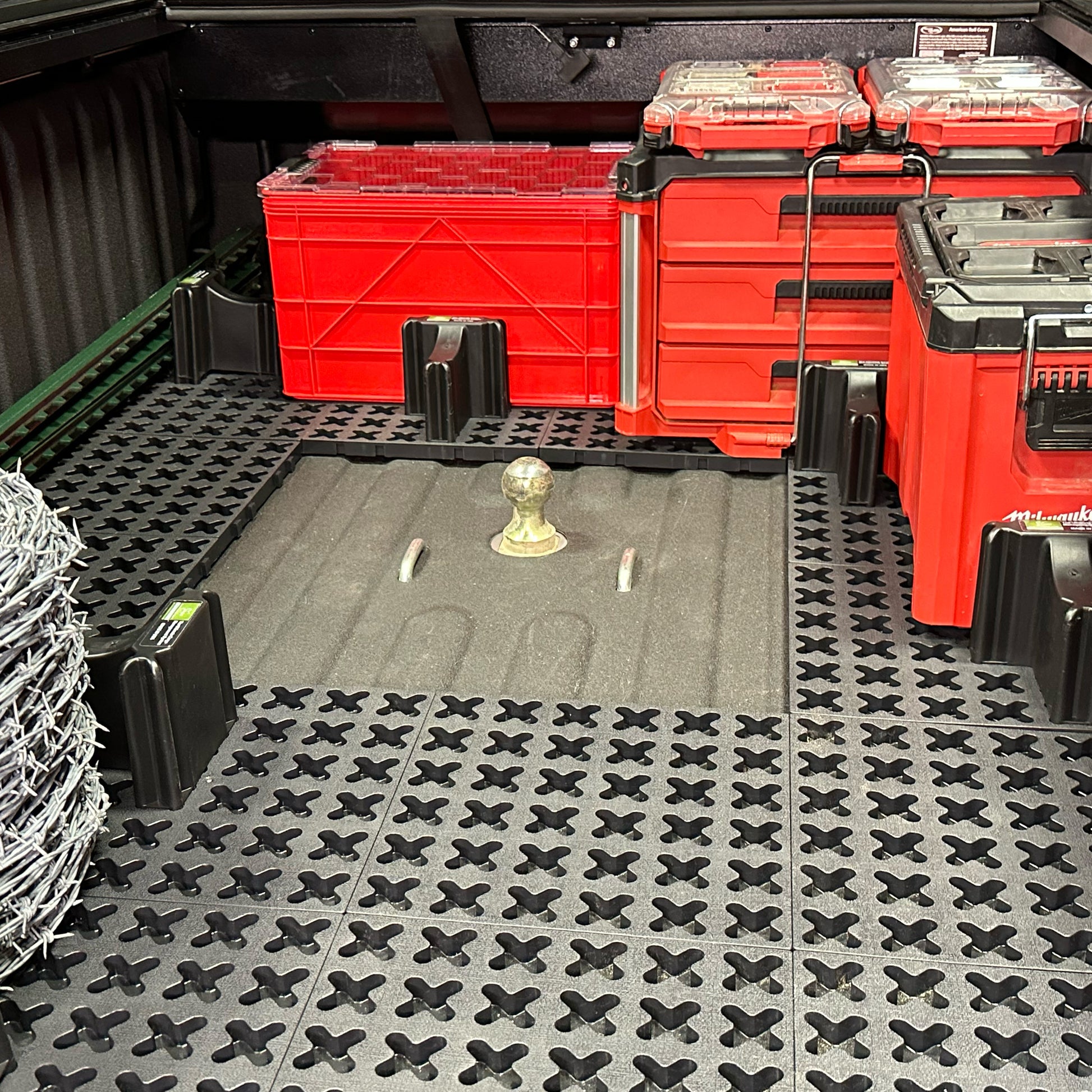 Packout tool boxes, a red milk crate, a spool of barb wire, and t-posts secured in a truck bed around a gooseneck hitch.