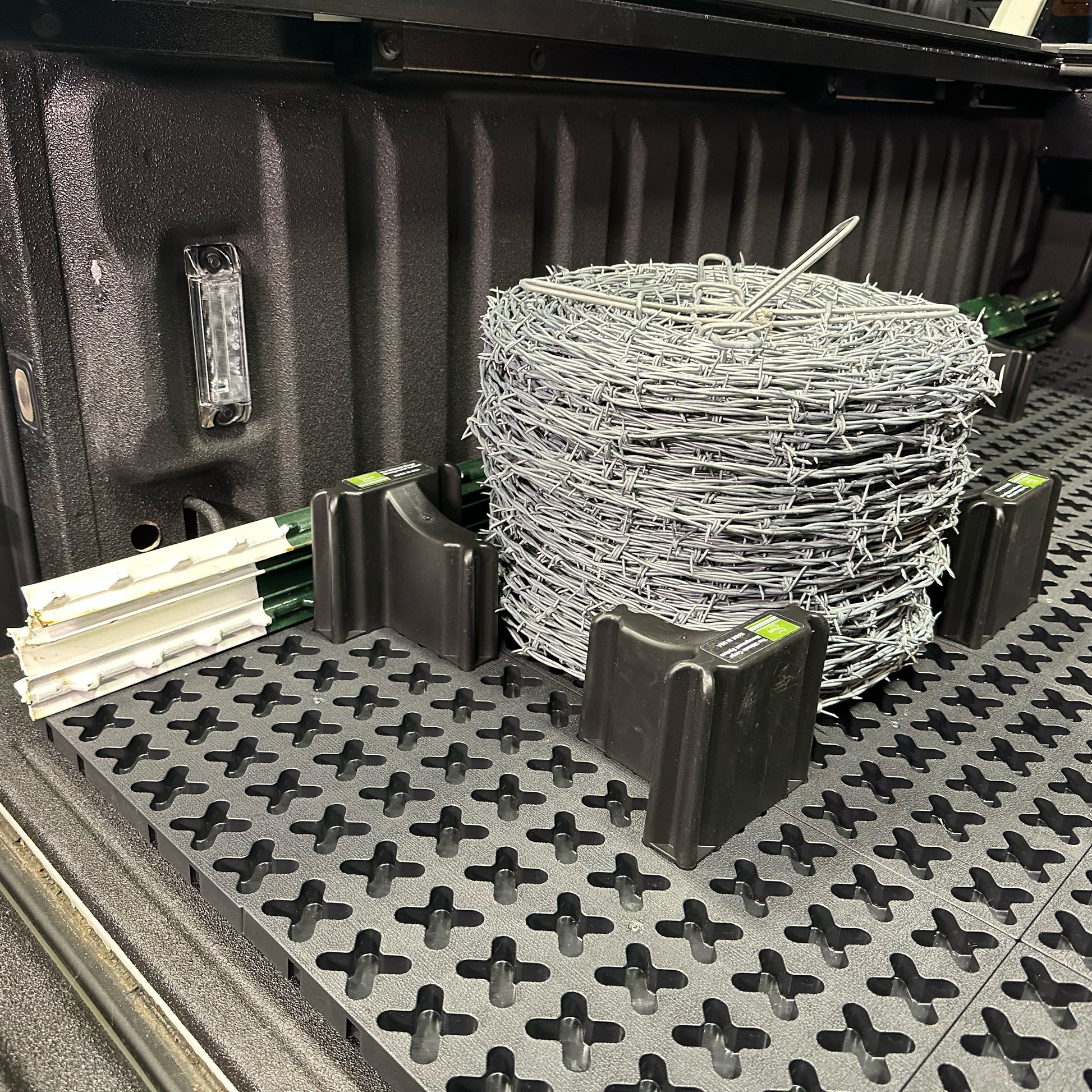 A spool of barbed wire and t-posts secured in a truck bed.