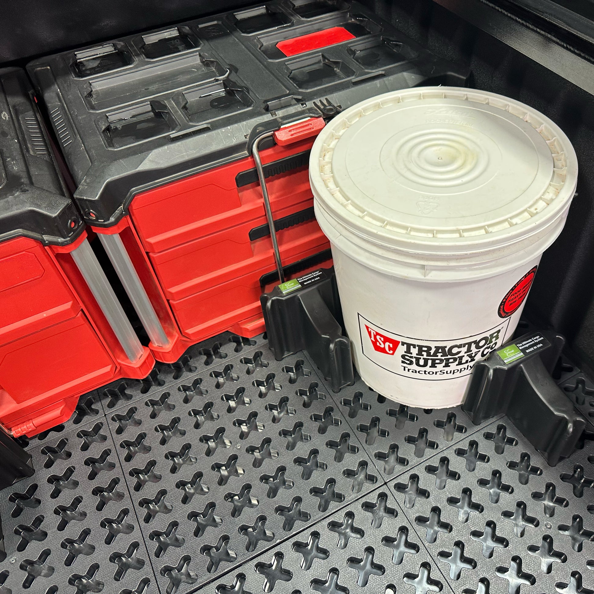 Two red toolboxes and a Tractor Supply bucket secured with Tmat Stationary Cargo Blockers.