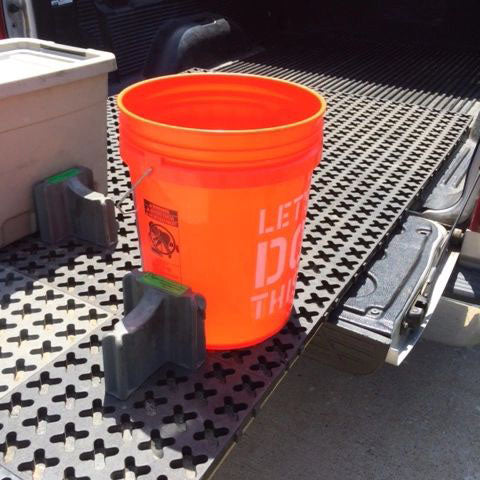 An orange 5-gallon bucket secured in a Tmat that is slid out over a tailgate.
