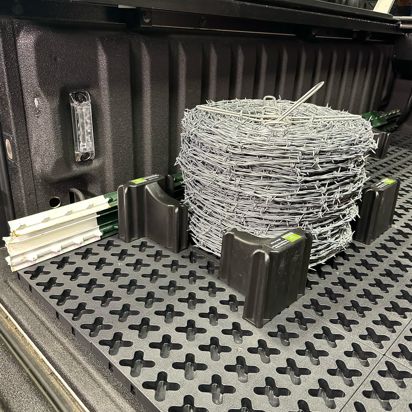 A spool of barb wire and t-posts secured in a truck bed.