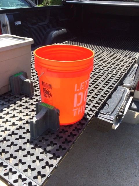 An orange 5-gallon bucket secured in a Tmat that is slid out over a tailgate.