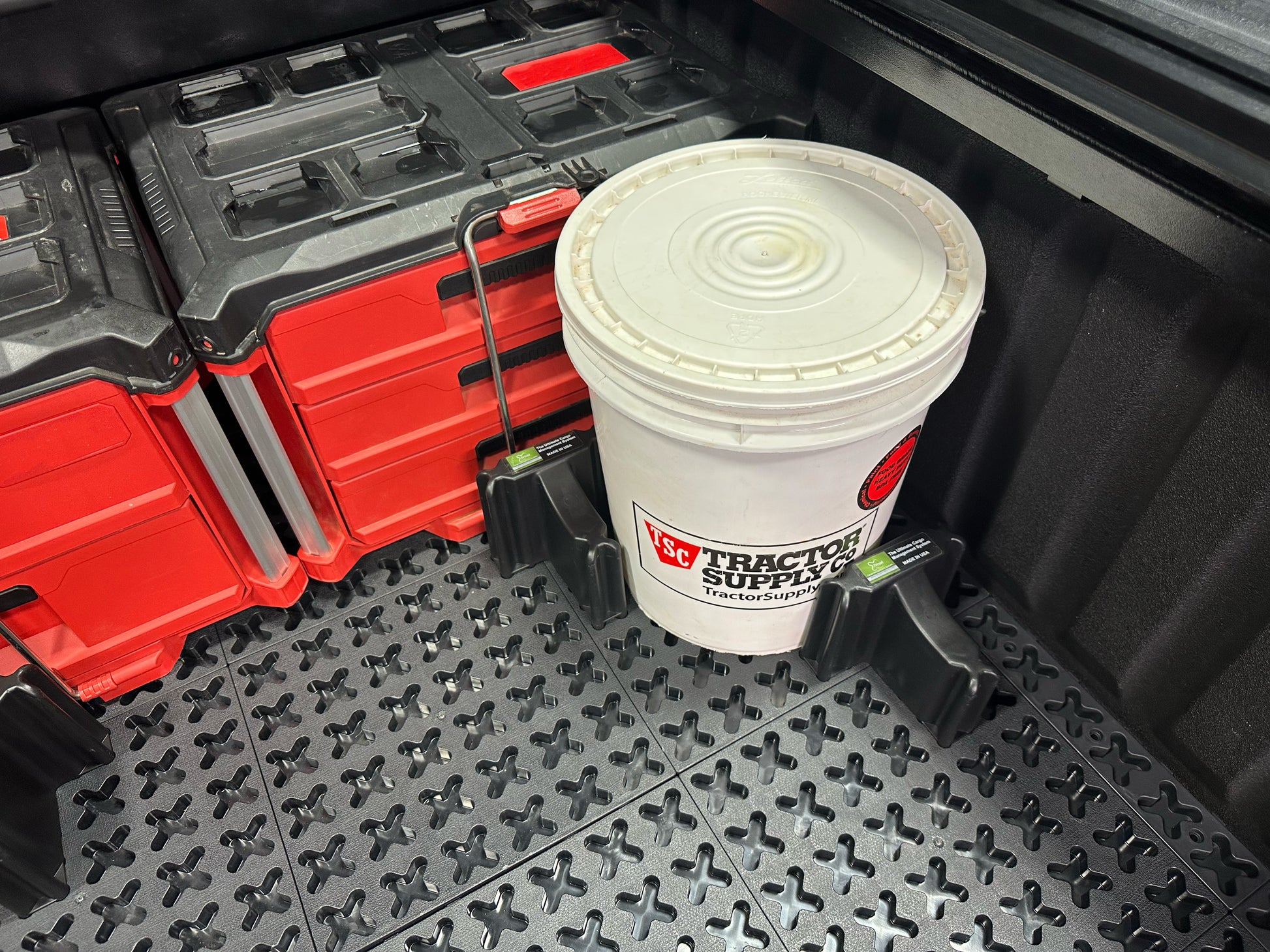 Two red tool boxes and a Tractor Supply bucket secured with Tmat Stationary Cargo Blockers.