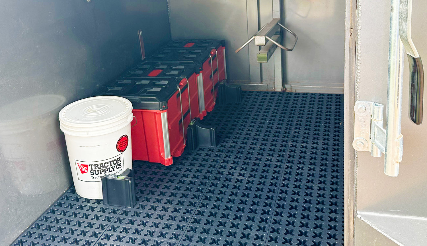 Tmat installed into the floor of a stock trailer tac room with two red toolboxes and a 5 gallon bucket.
